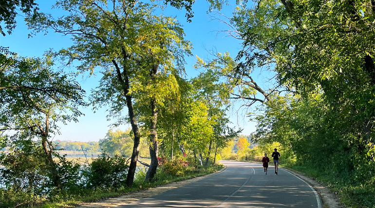 Two people going for a run on a paved path in the arboretum.