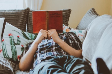 person laying couch reading pillows curtains