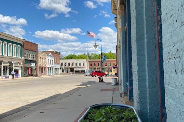 A street with buildings, cars, planters, and an American flag.