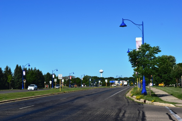 A street with cars, trees, light posts, and a water tower in the distance. 