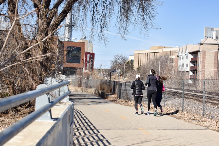 Three people in parkas jogging on a paved trail in winter.