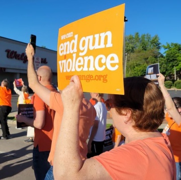 A picture from a rally on a sunny summer day. Someone holds a sign that says we can end gun violence