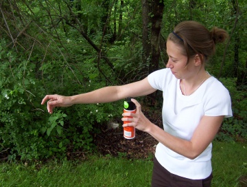 A person sprays their body with bug spray