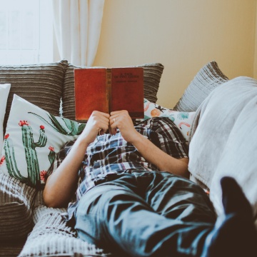 person laying couch reading pillows curtains