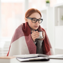 Person sitting at a table drinking coffee and looking at laptop.