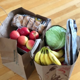 paper bags of apples, bananas, cabbage, bagels, and bread from a grocery store